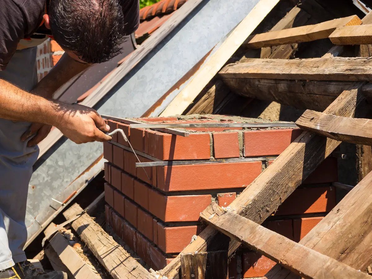 Mason rebuilding a brick chimney stack on a roof