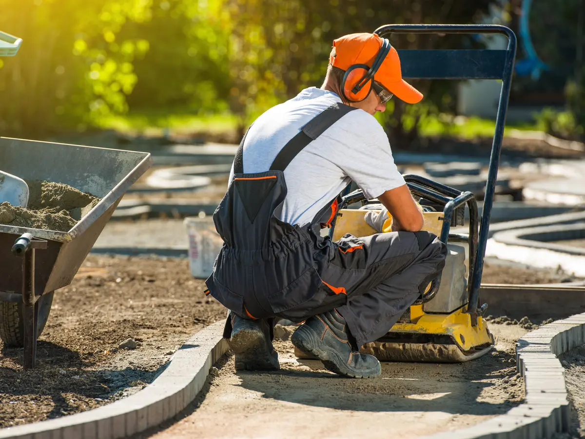 Worker preparing a compacted base for pavers with a plate compactor