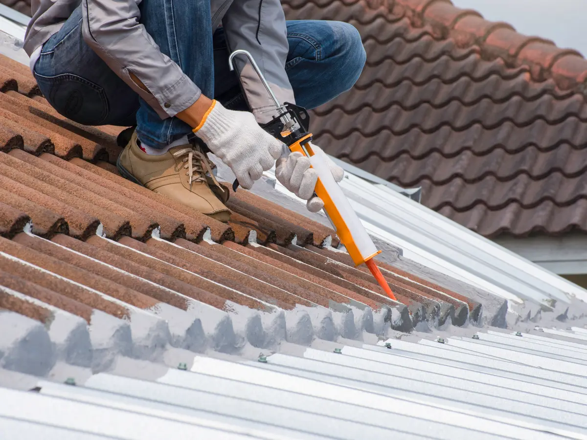 Roofer sealing a joint on a concrete tile roof with a caulking gun