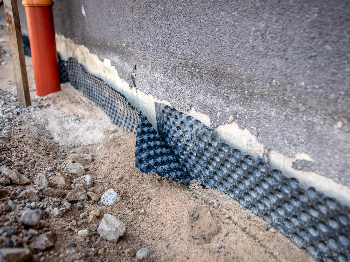 Dimpled drainage membrane fixed to a foundation wall above gravel