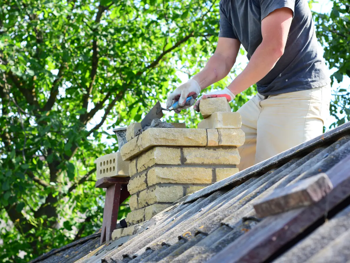 Mason laying bricks to rebuild a chimney stack on a roof