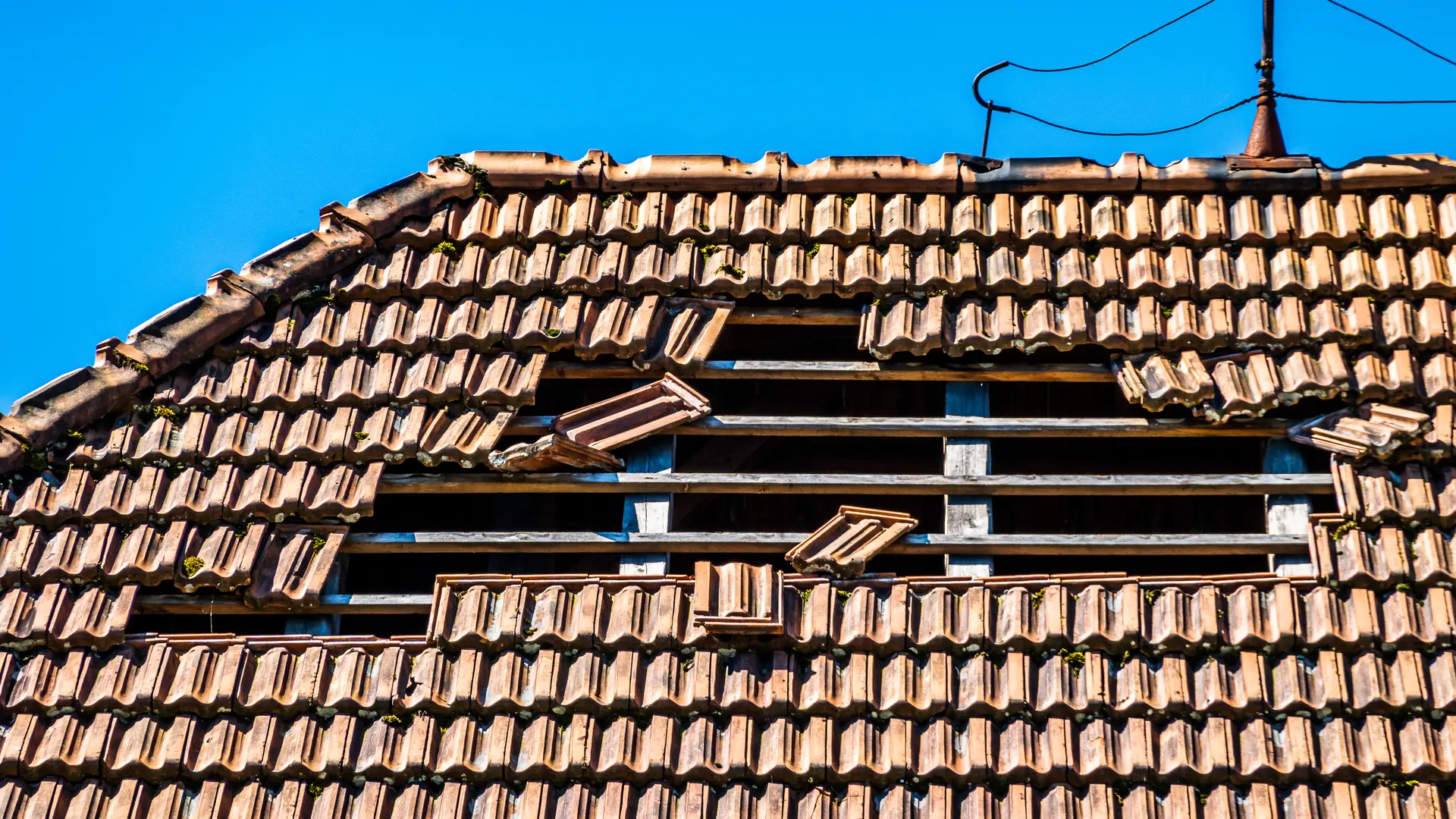 Hole torn through a tile roof by storm winds, with loose tiles around it