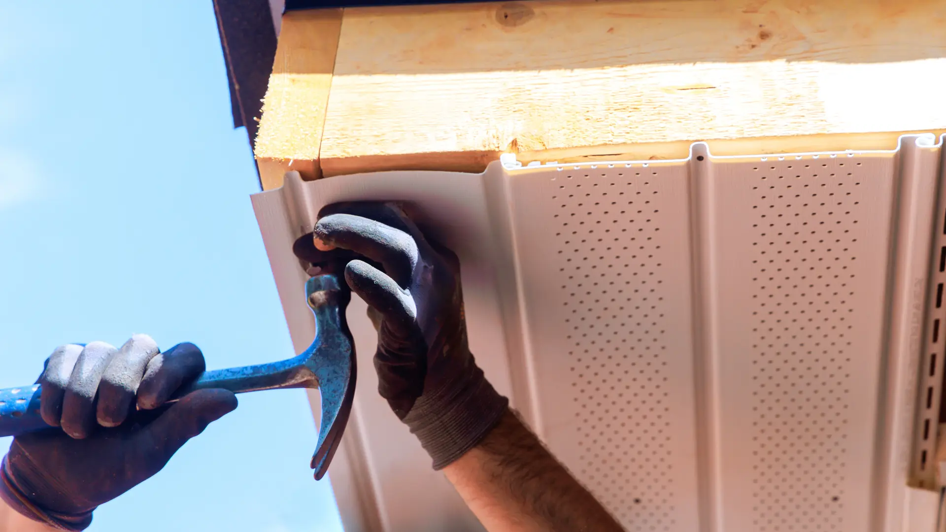 Installer nailing a vented soffit panel under the eaves