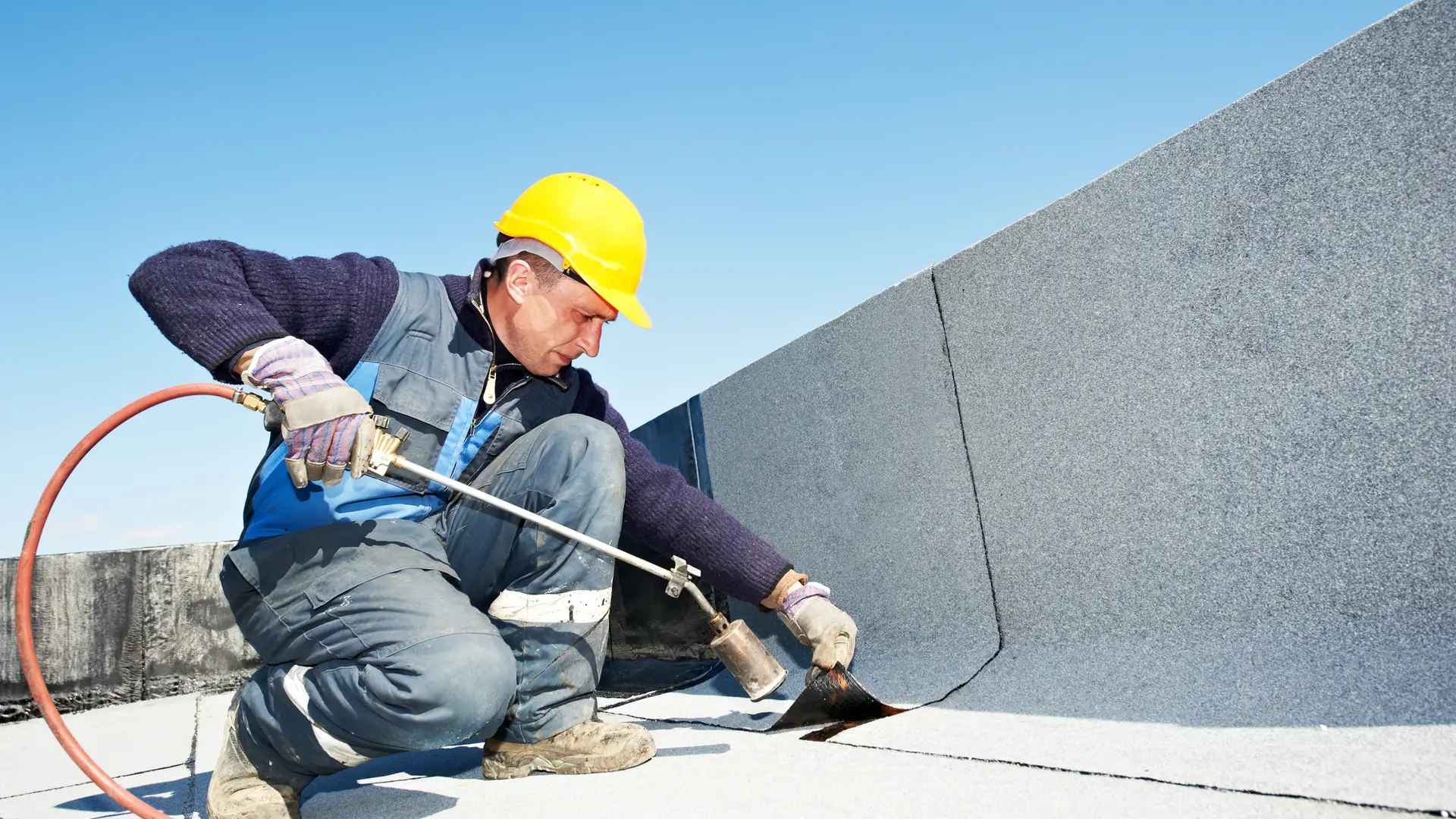 Roofer heat-sealing a membrane up the parapet of a flat roof