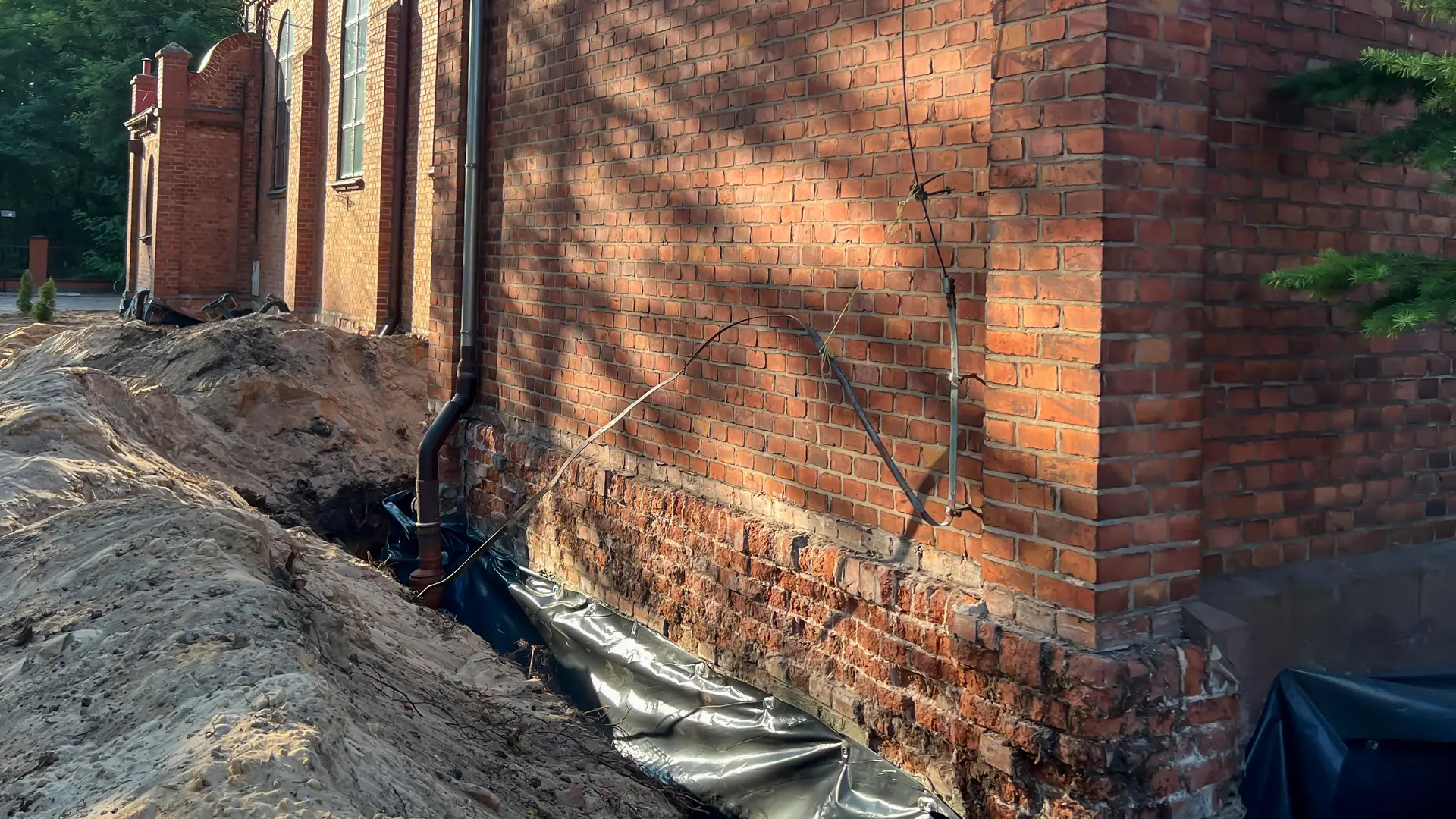 Excavated brick foundation wall with a waterproof membrane being laid