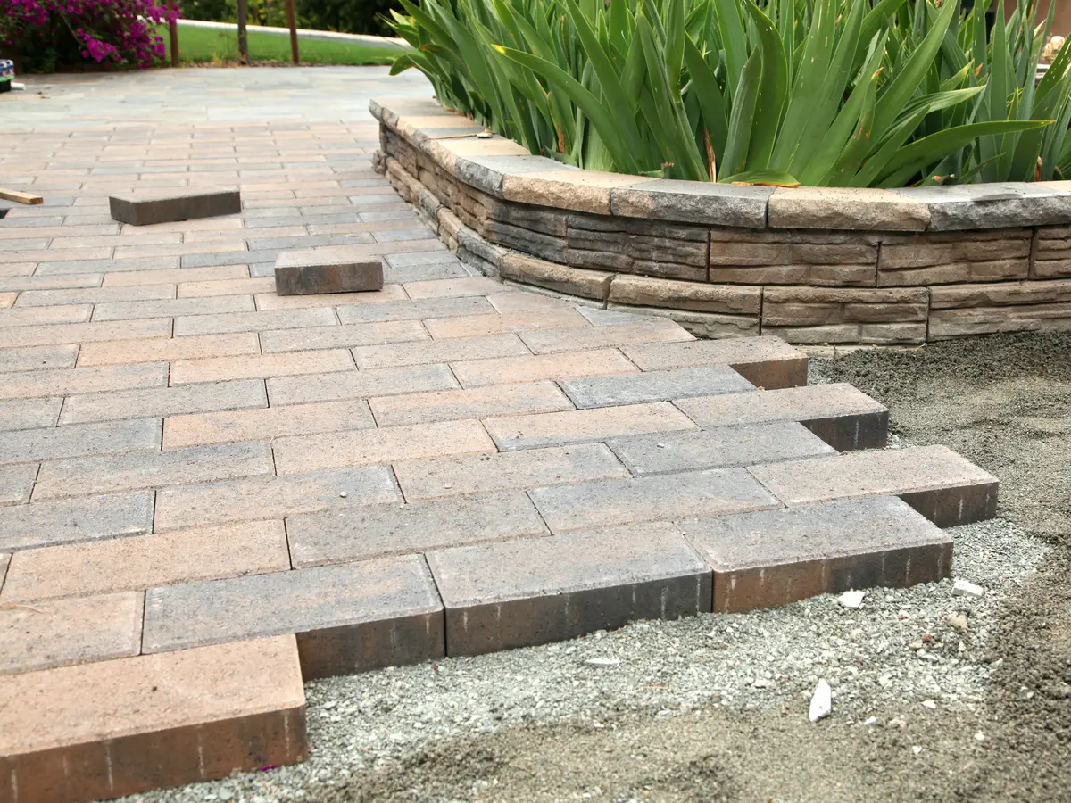 Pavers being laid on a prepared base beside a curved stone wall