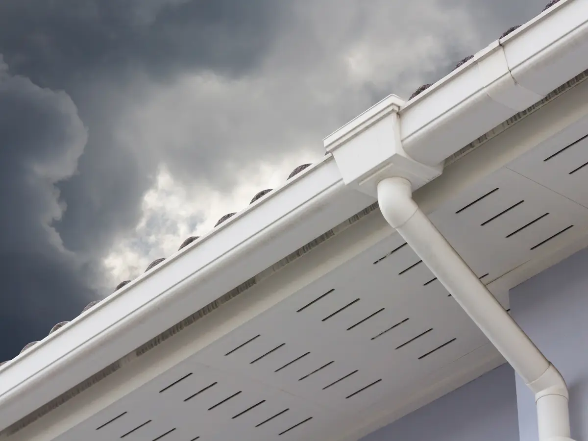 White vented soffit, eavestrough and downspout under a stormy sky