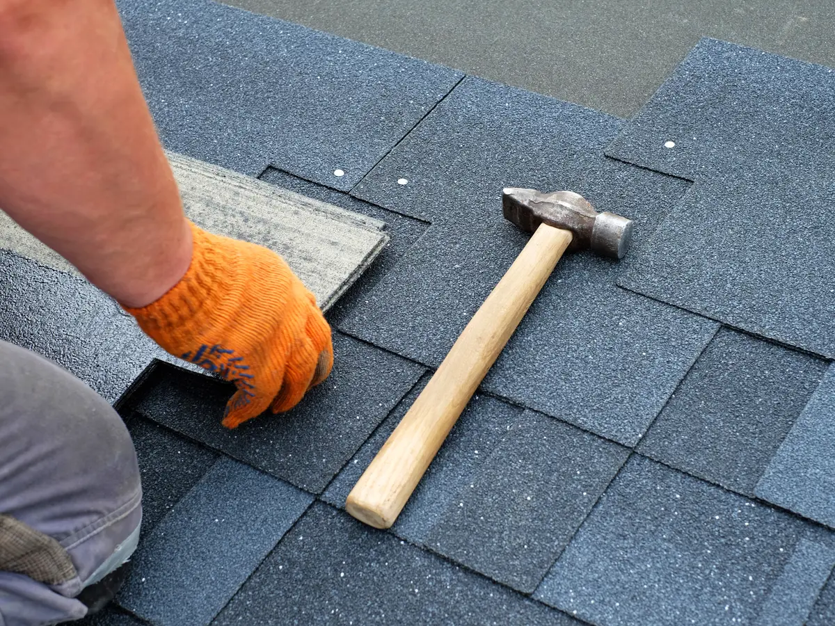 Roofer nailing a new asphalt shingle in place with a hammer