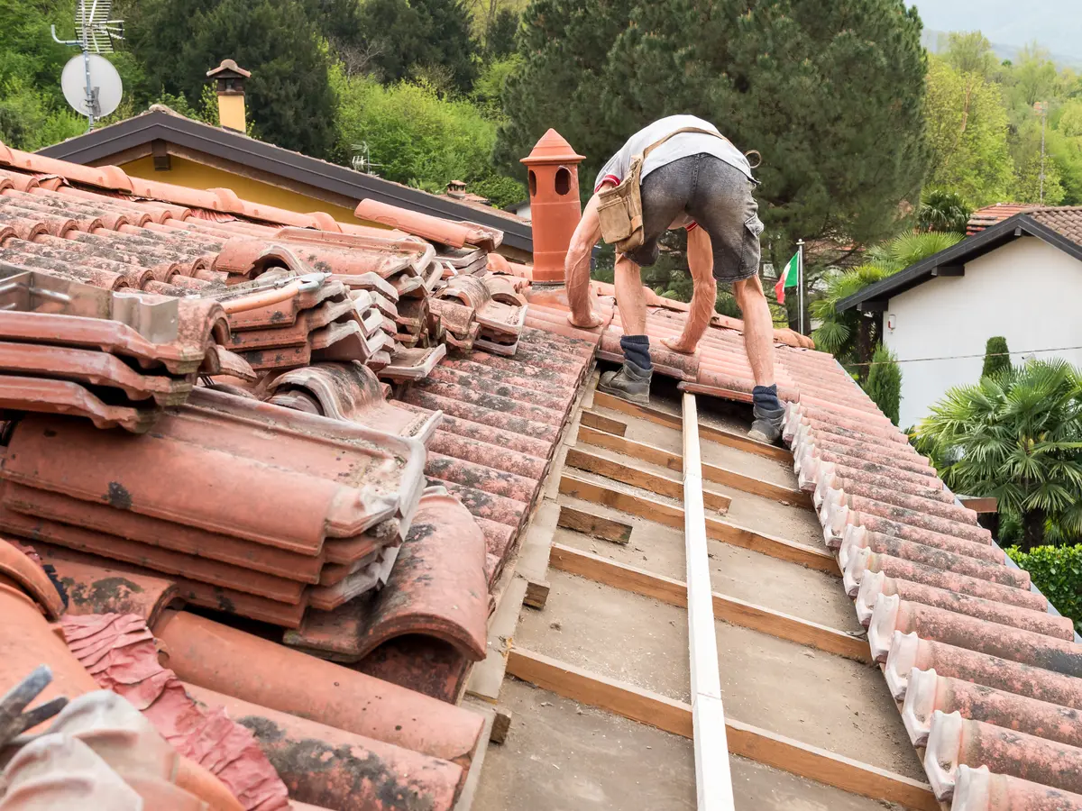 Roofer relaying clay tiles on new battens